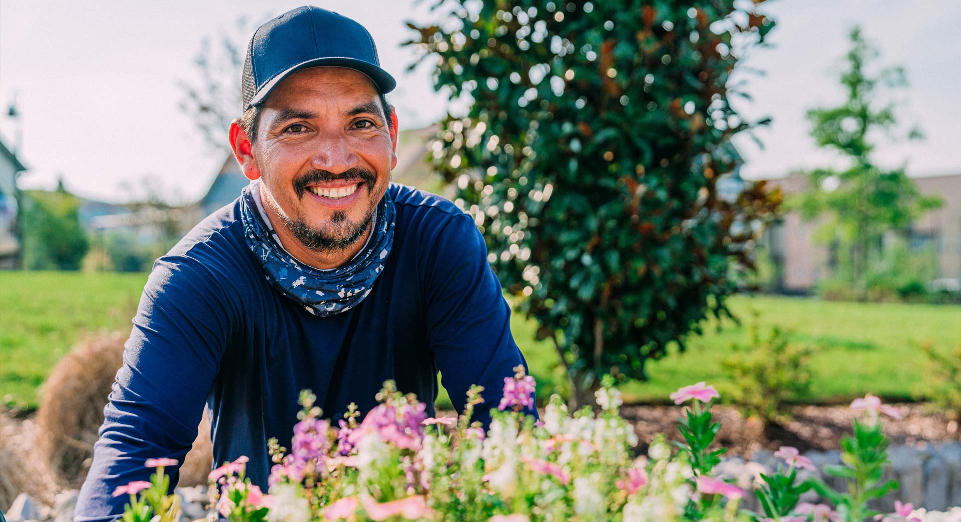 A gardener smiles next to his flower garden