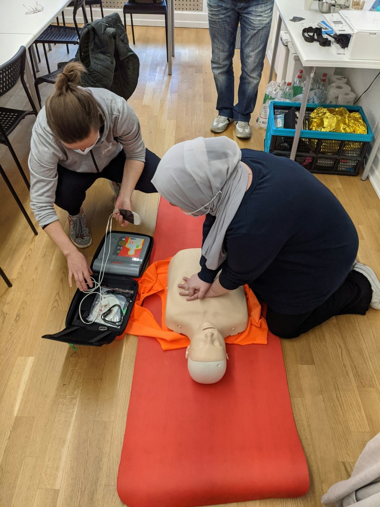 Instructor teaching a woman to perform CPR on a test dummy in a classroom