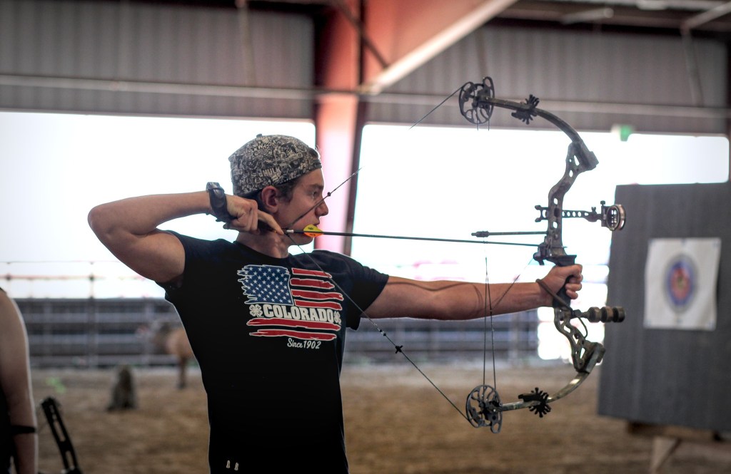 A teen points a compound bow and arrow at a target during a competition