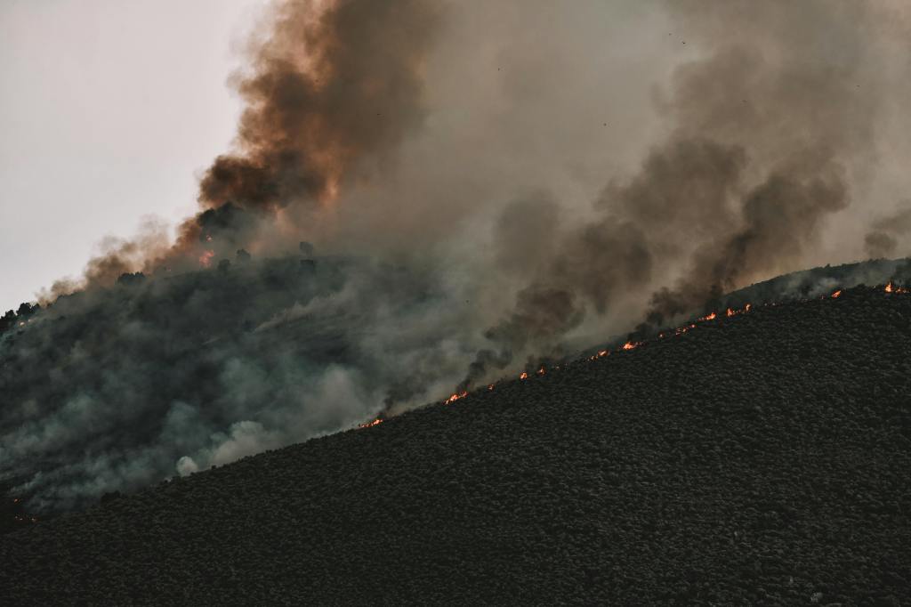 dark smoke billows from a wildfire on a mountainside