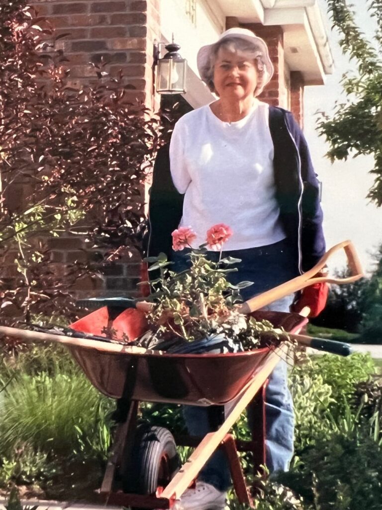 Barbara at her home garden using a wheelbarrow to hold her flowers and gardening tools.