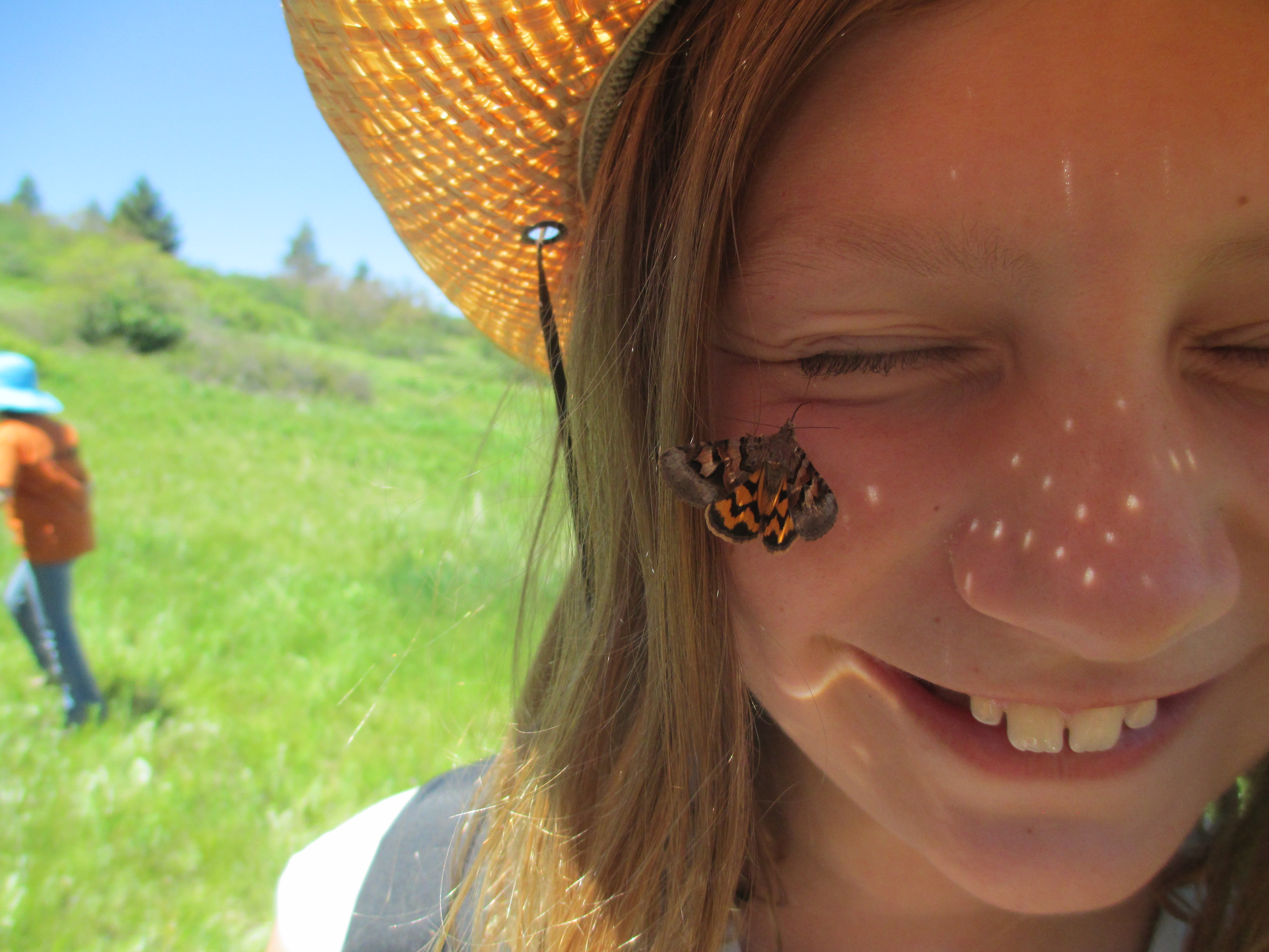 A child smiles at the camera with a butterfly on her cheek.