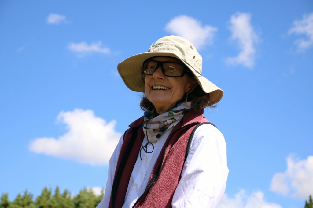 An older woman smiles into the distance, a blue sky behind her.
