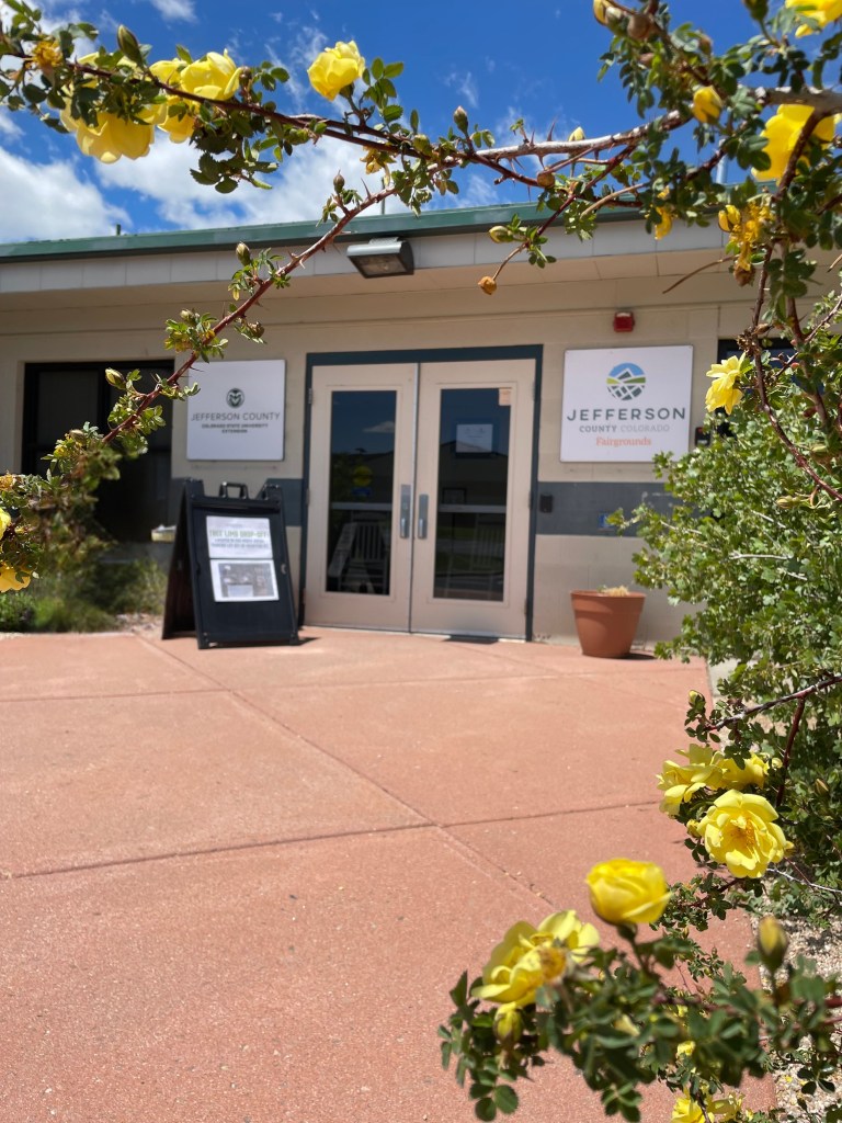 Front doors of the CSU Extension offices, framed with a flower growing in the garden.  Linked to link to Jeffco Parks and Open Space website.