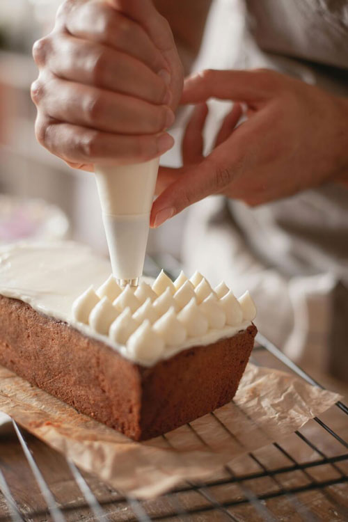 a close up photos of handles applying frosting dots to a small cake made in a loaf pan