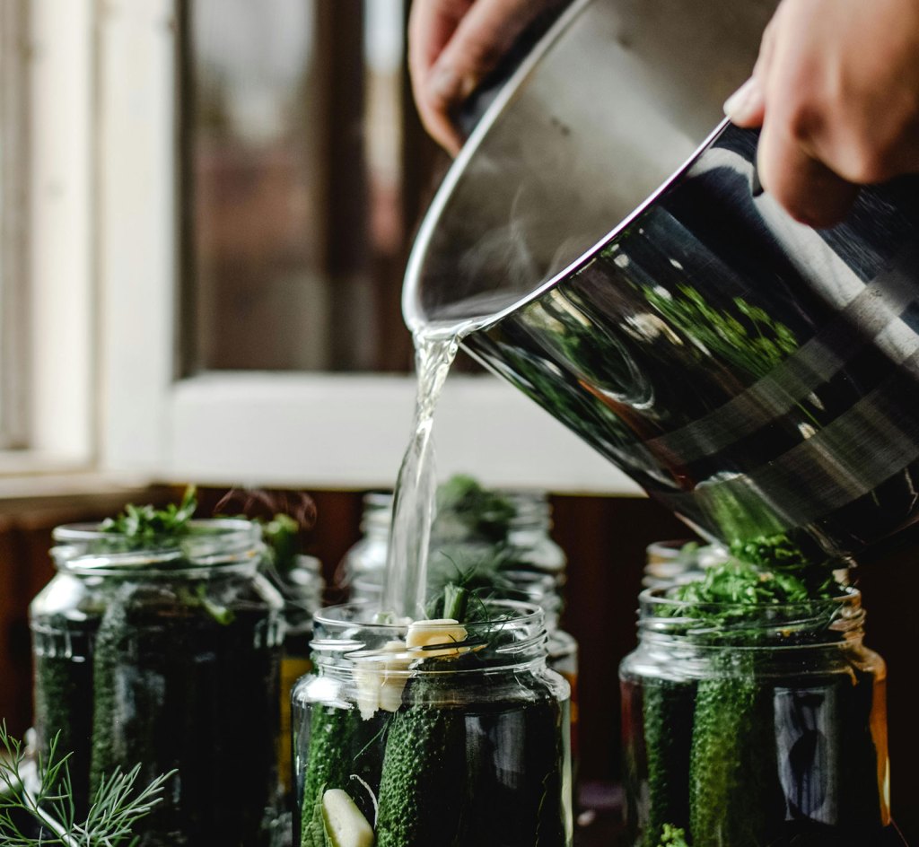 A person pours hot liquid into a jar of pickles