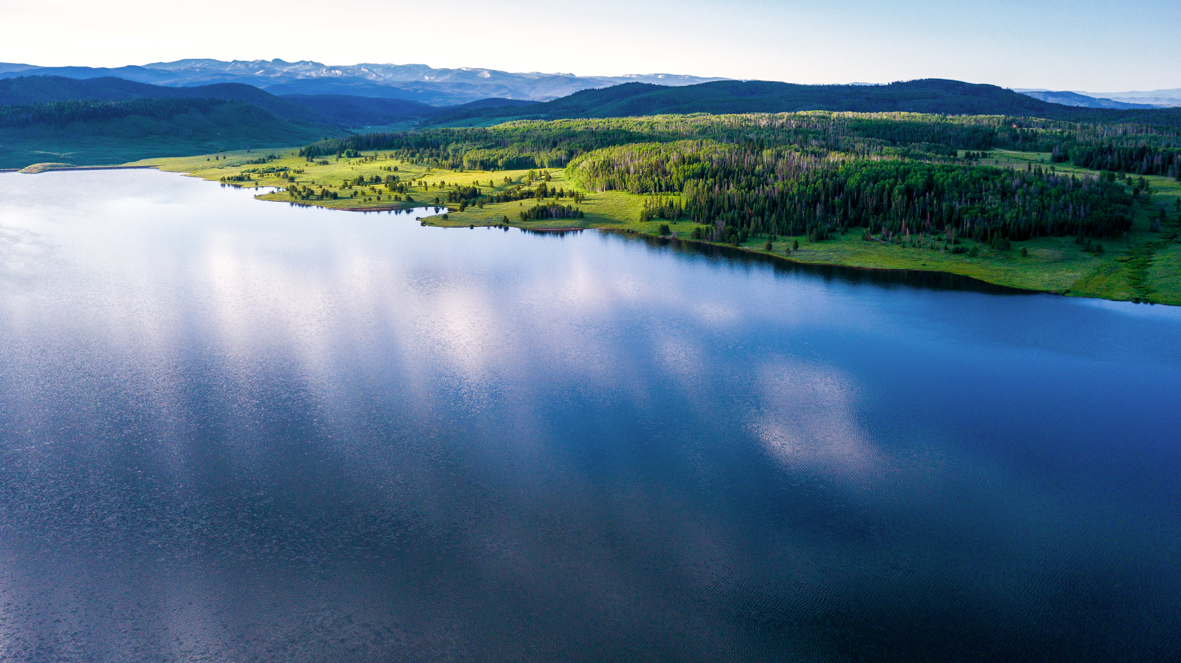 broad view of a lake with green forest and mountains in the background