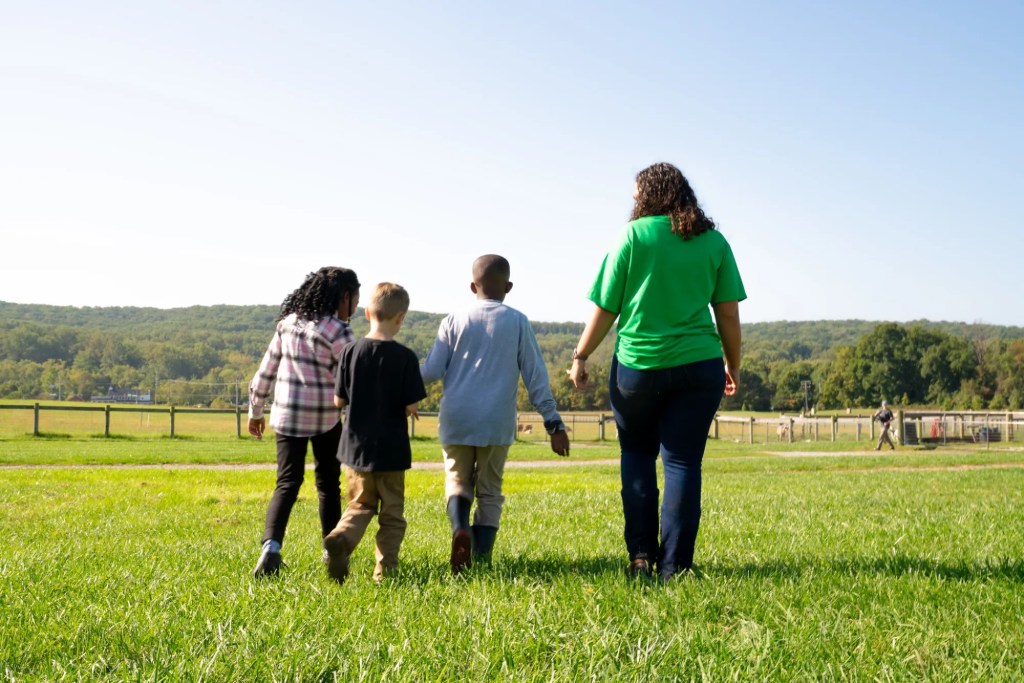 A 4-H adult leader walks with youth through a green grassy field