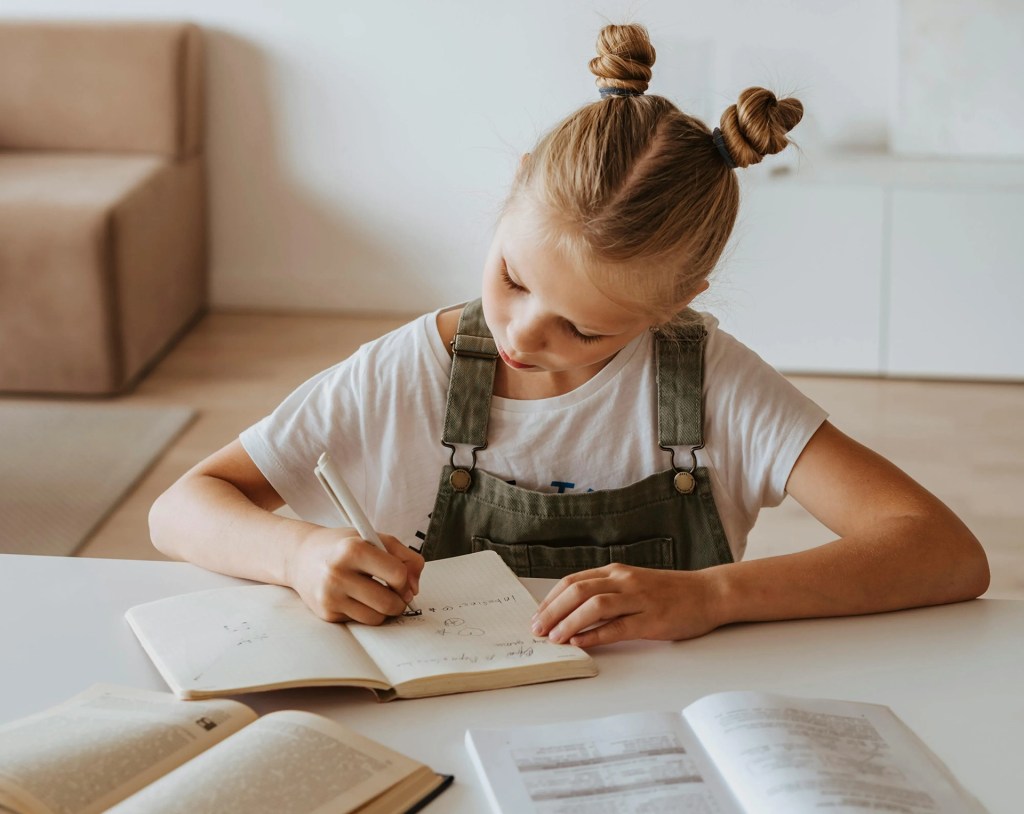 A young girl writes in a notebook at a table