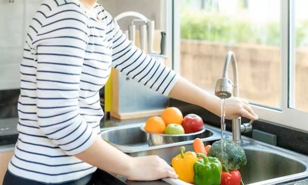 A person wearing a black and white striped shirt cleaning vegetables at a kitchen sink
