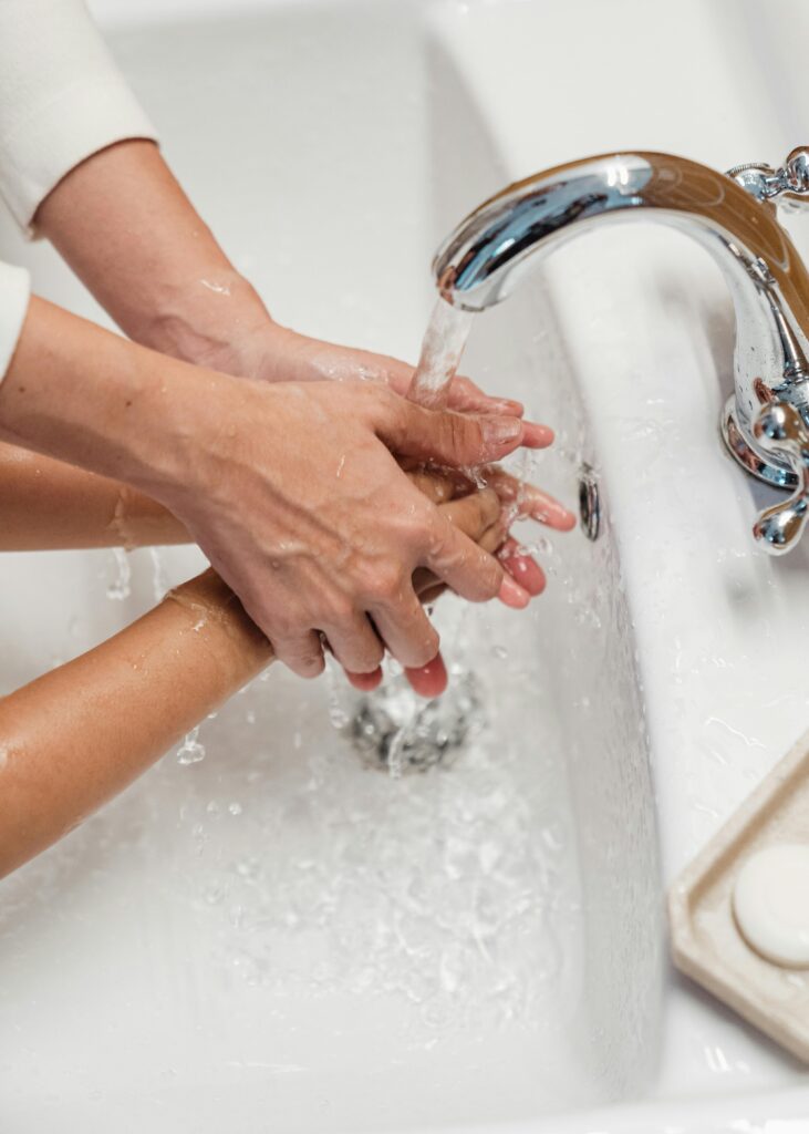 Close up of 2 people washing their hands in the sink.