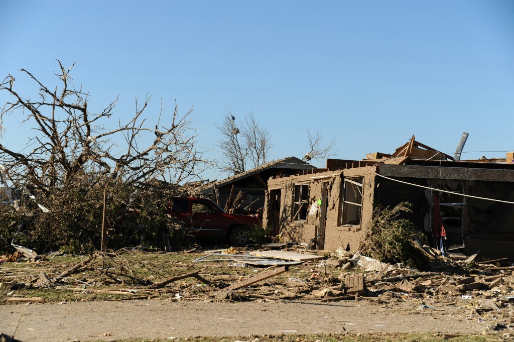 Damaged homes and trees after a natural disaster, with debris scattered across the ground.