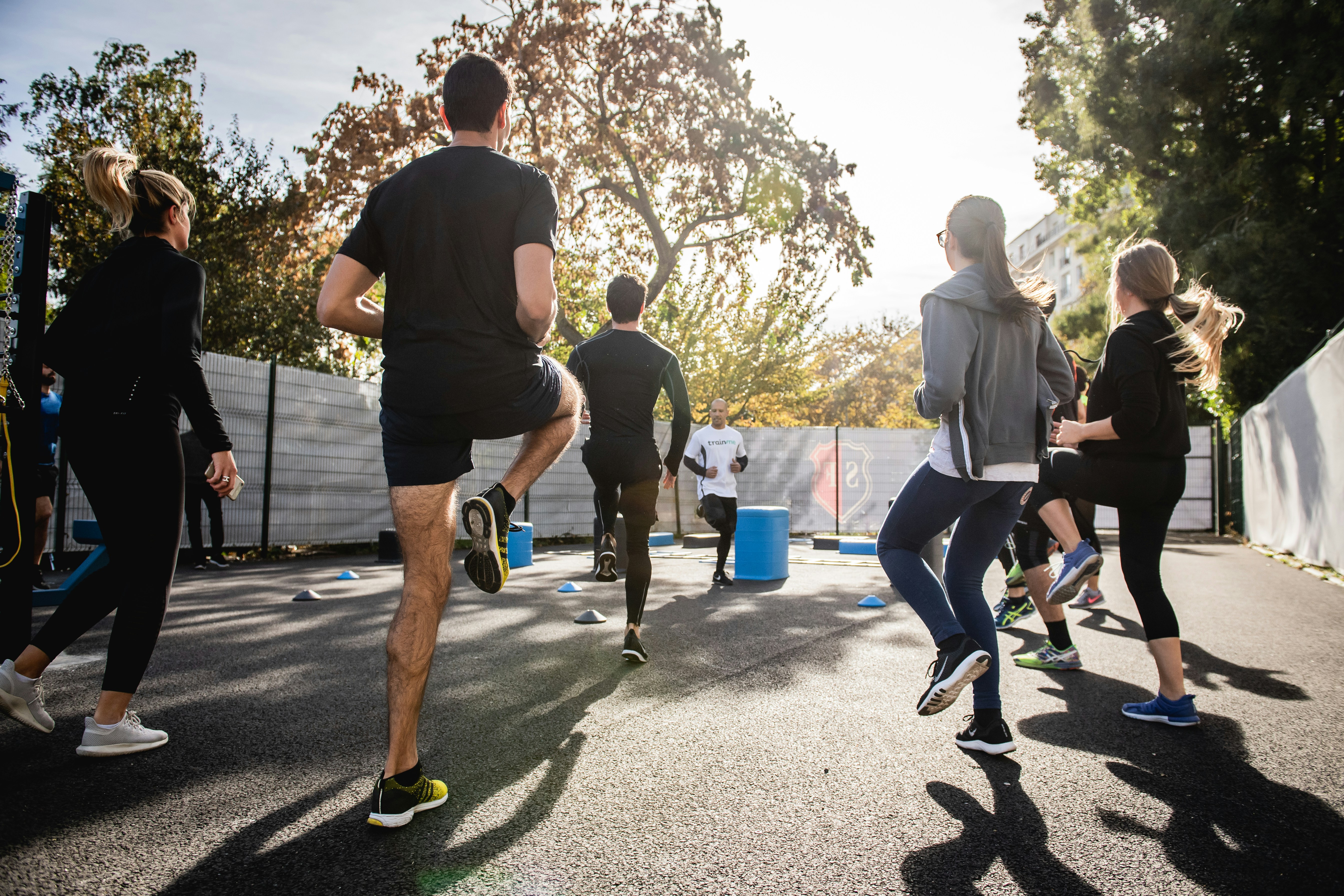 A group of people exercises outdoors together, following an instructor during a fitness class.