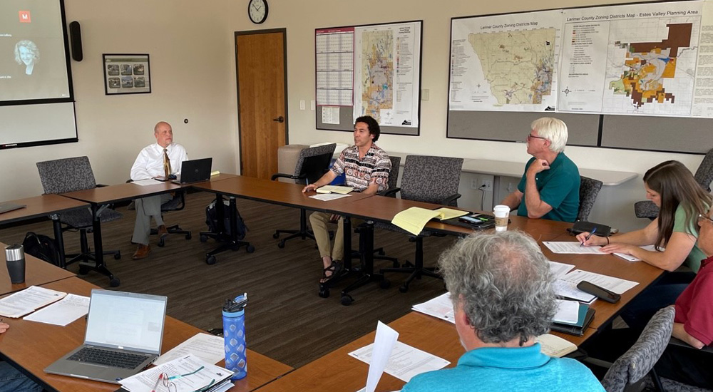 Six people seasted around a conference table with laptops, notepads, and water bottles, while Caesar Garduno, MPPA student, speaks to the group. Behind them on the wall are various maps and charts.