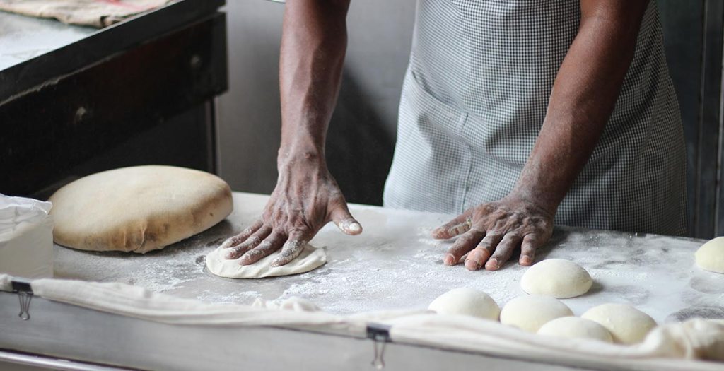 Close up of hands kneading pieces of dough on a floured countertop.