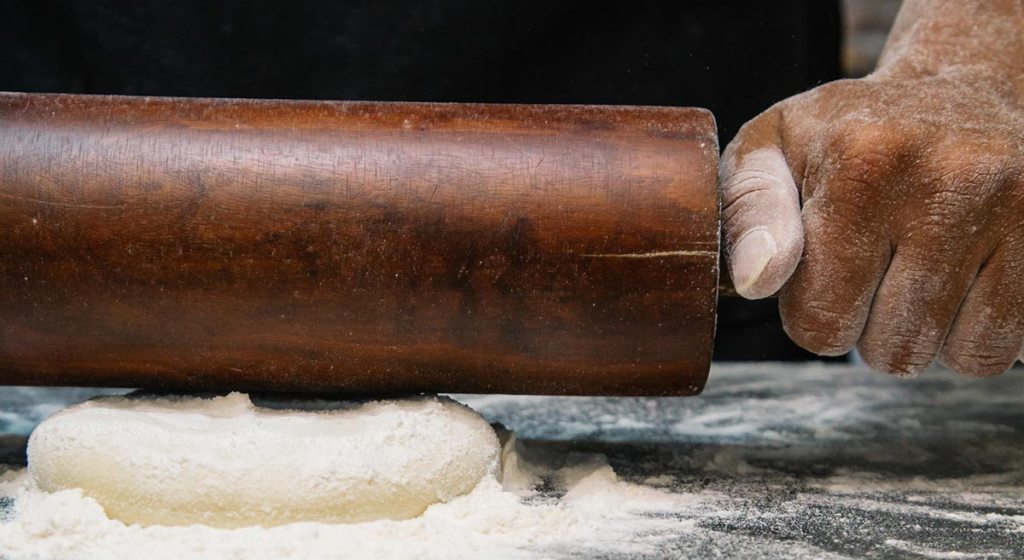 Closeup of a piece of dough being rolled out with a wooden rolling pin.