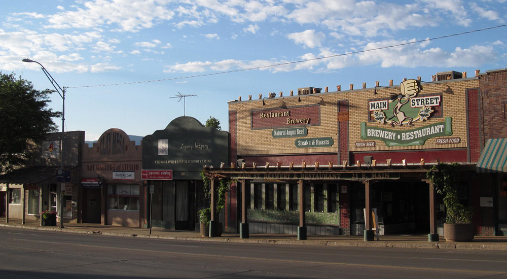 Street view of several store fronts, with 'Main Street Brewery and Restaurant' prominently featured and signs advertising steaks, roasts, and fresh food. Nearby are signs for Legacy Imagery and and Art Gallery & Studio.