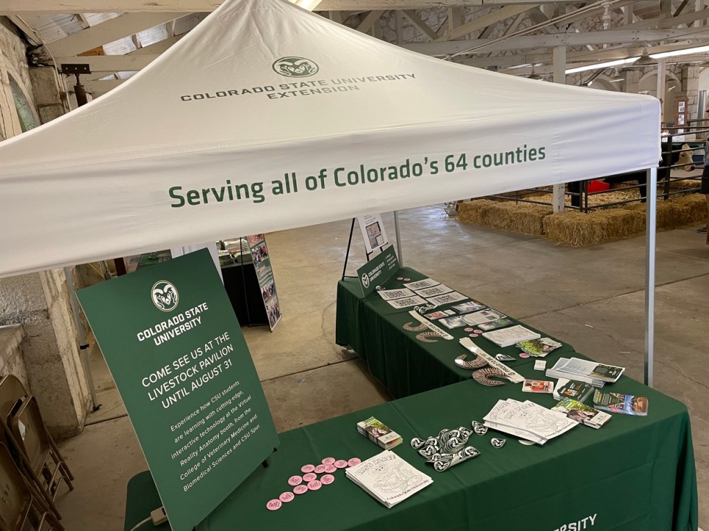 A Colorado State University Extension pop-up tent set up over tables that have brochures, stickers, pins, and other information pamphlets used for an educational demonstration at the Colorado State Fair.