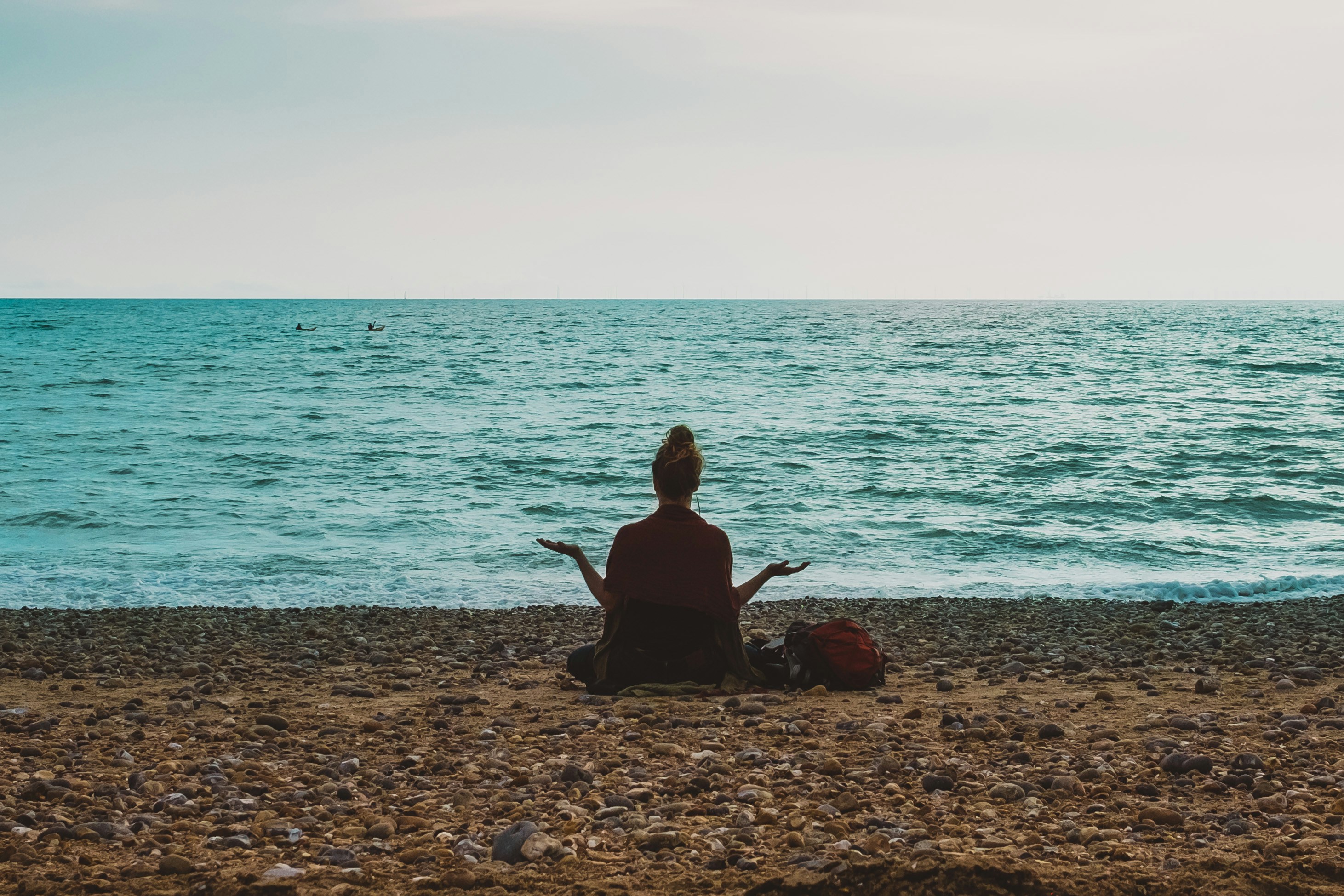 A person sits cross-legged on a rocky beach, meditating while facing the ocean.