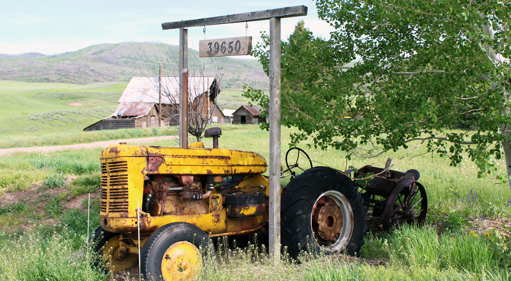 Old, yellow tractor parked underneath a wooden address sign at the Stanko Ranch.
