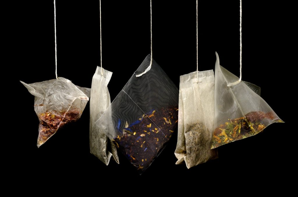 Various bags of tea, herbs, and spices hanging down against a black background.