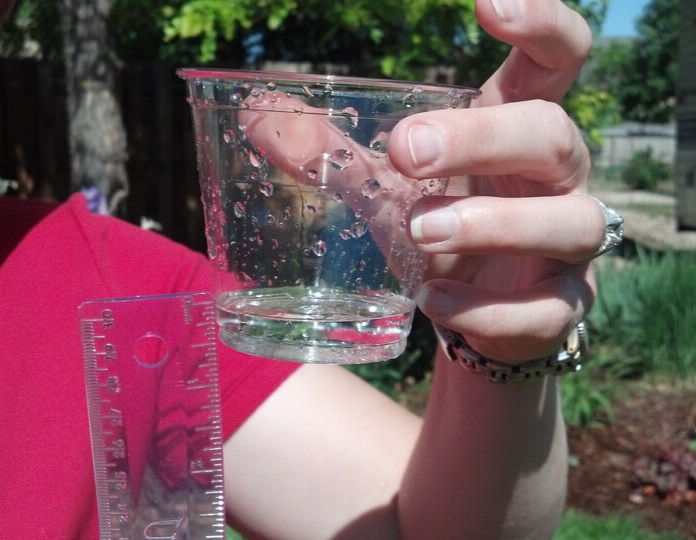 Person using a ruler to measure the water level collected in a plastic cup after an informal lawn irrigation audit is complete.
