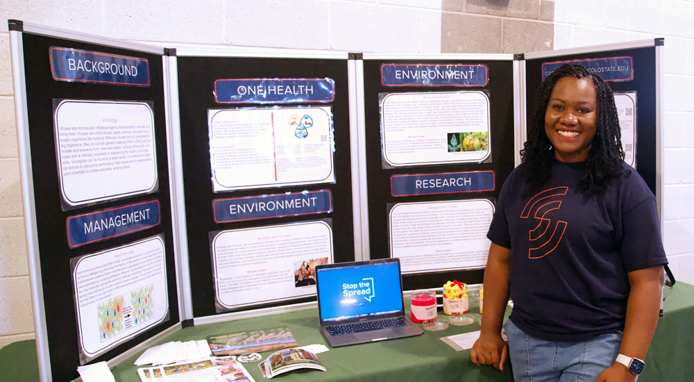 Joy Enyinnaya smiling in front of her poster showcasing vaccination hesitancy.