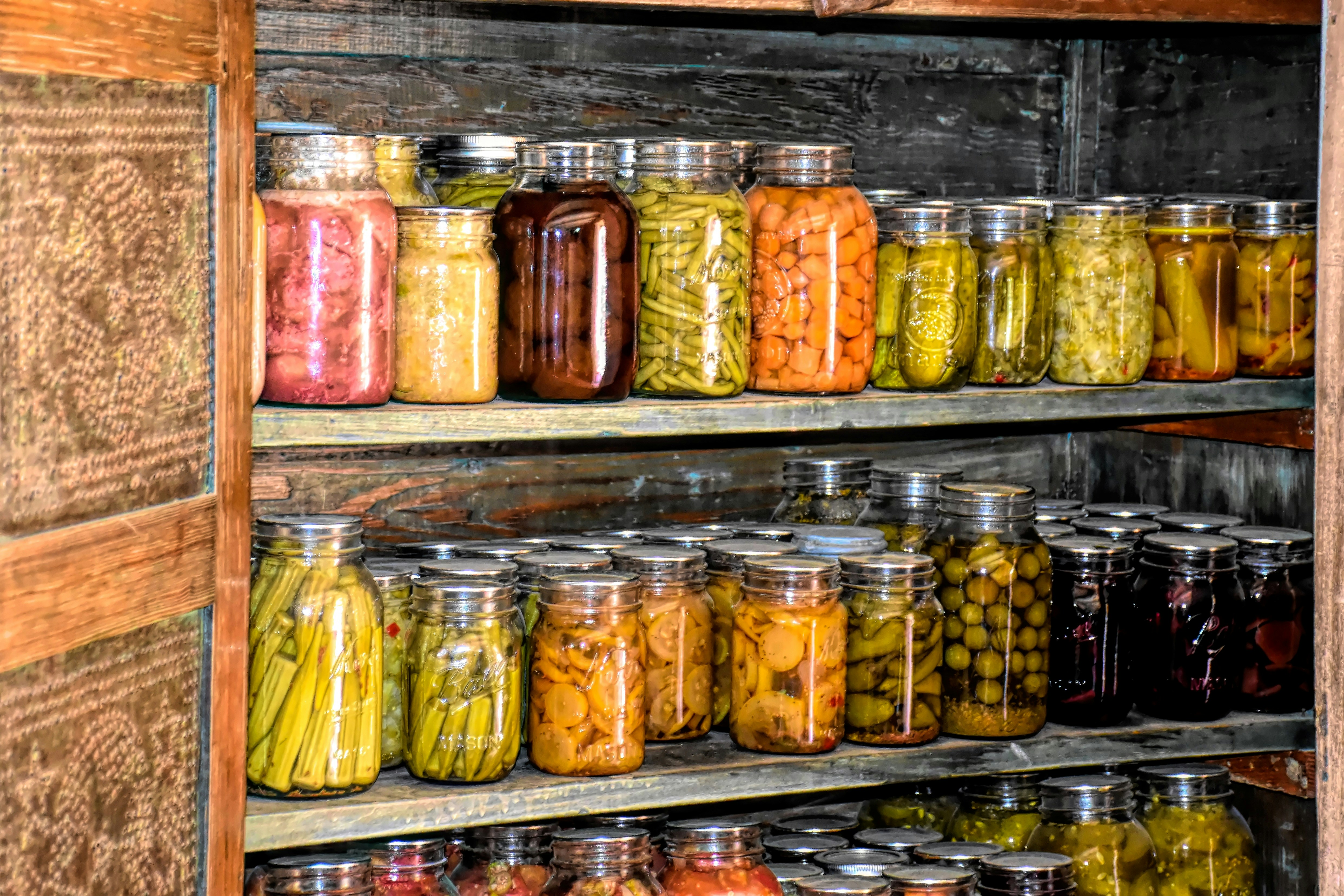 Shelves filled with glass jars of home-canned vegetables and pickles, organized in rows inside a rustic wooden pantry.