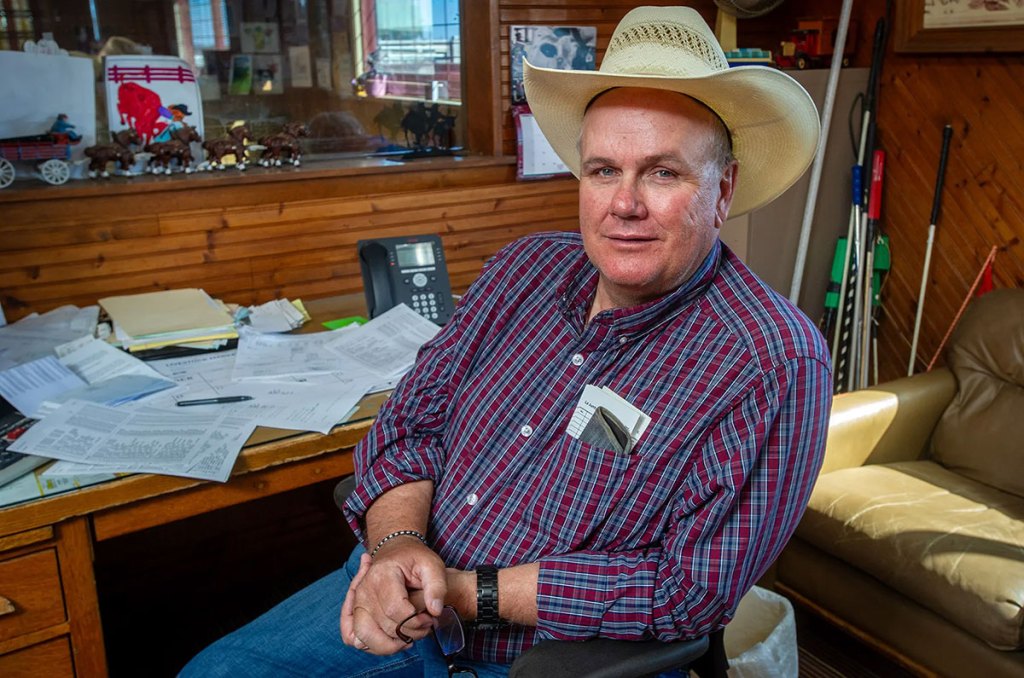 A man in a cowboy hat sits at a desk covered in paperwork