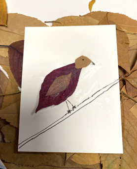 Artwork of a bird crafted from layered autumn leaves glued onto paper, with a drawn branch beneath the bird.