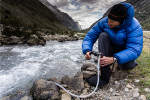 a backpacker uses a filter pump to get water from a stream