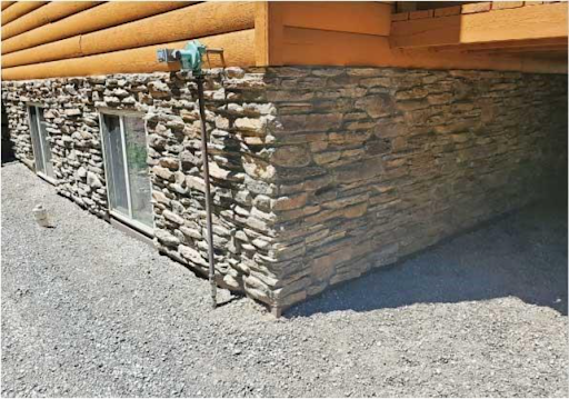 Wooden cabin with a stone foundation with a gravel ground surrounding.