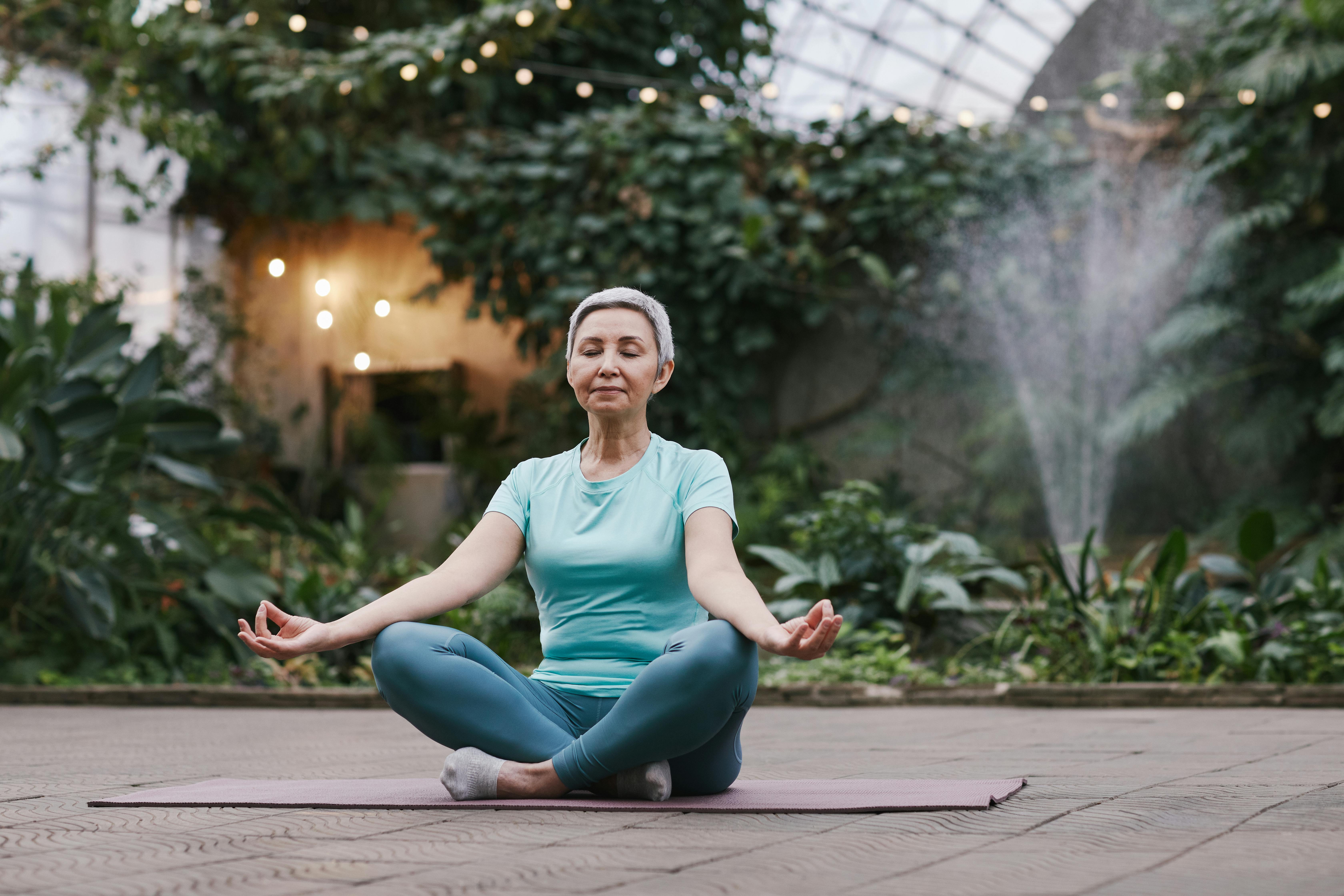 woman meditates on a yoga mat with plants and green bushes in the background