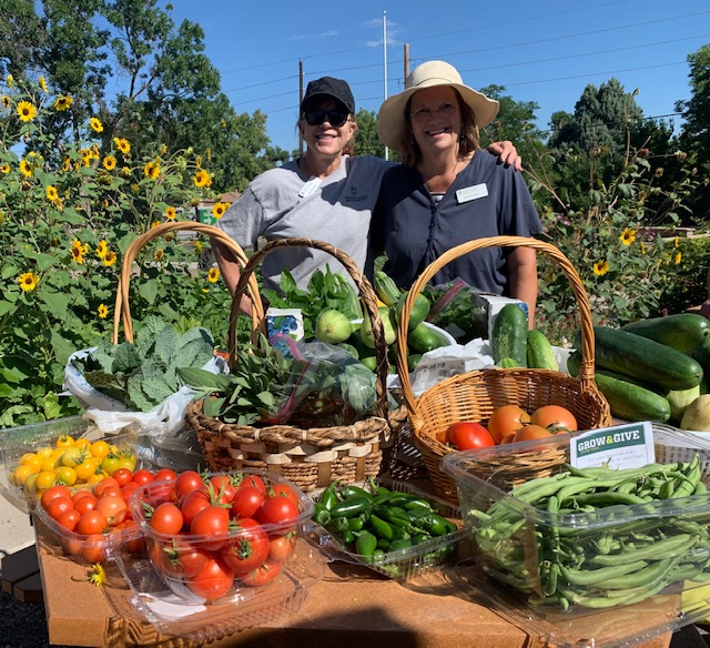 Two people standing behind a table filled with baskets and containers of fresh garden produce.