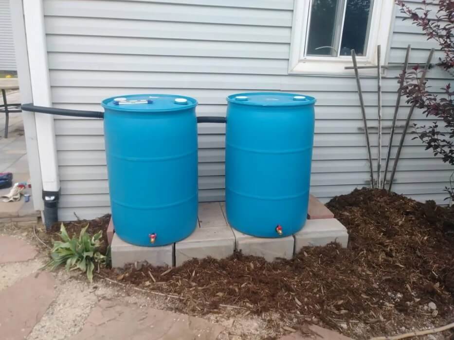 Two blue rain barrels sit next to a house.