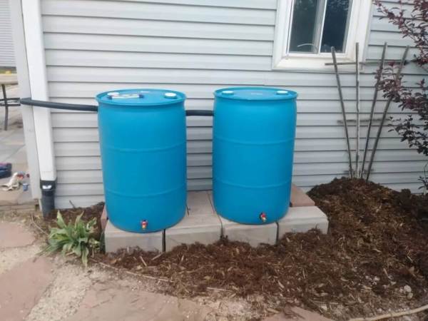 Two blue rain barrels sit next to a house.