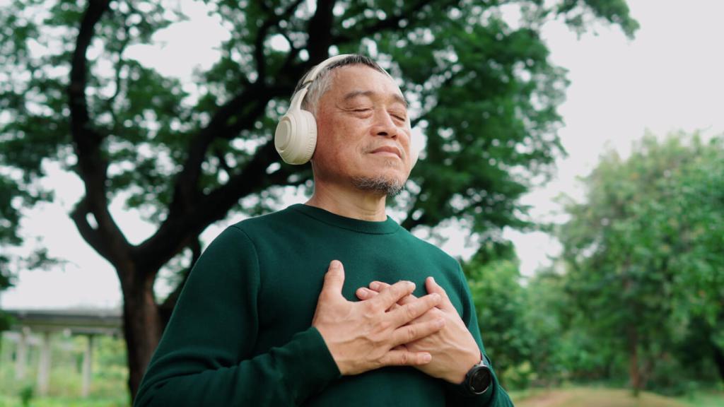 A person standing outdoors in a park setting wears headphones and places both hands over the chest, with large trees and greenery in the background.