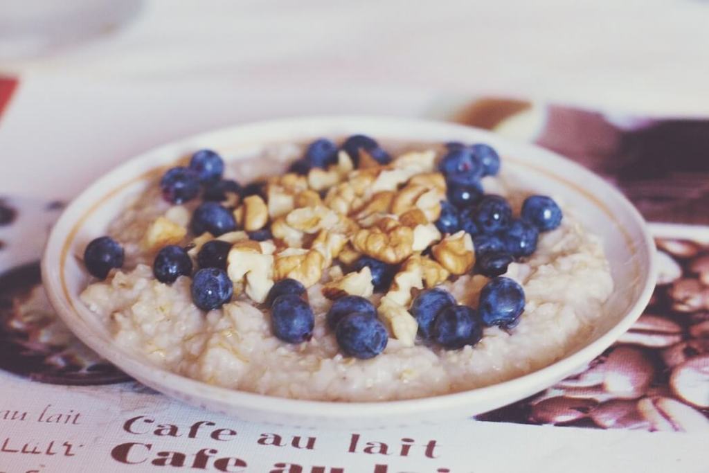 A bowl of oatmeal topped with blueberries and chopped walnuts, placed on a table with a softly blurred background.
