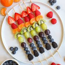 Colorful fruit skewers made with strawberries, kiwi, grapes, blackberries, and blueberries arranged on a white plate.