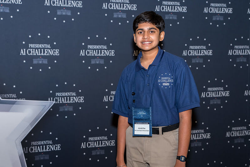Anirudh Rao standing in front of a blue backdrop that says "Presidential AI Challenge" in Washington D.C