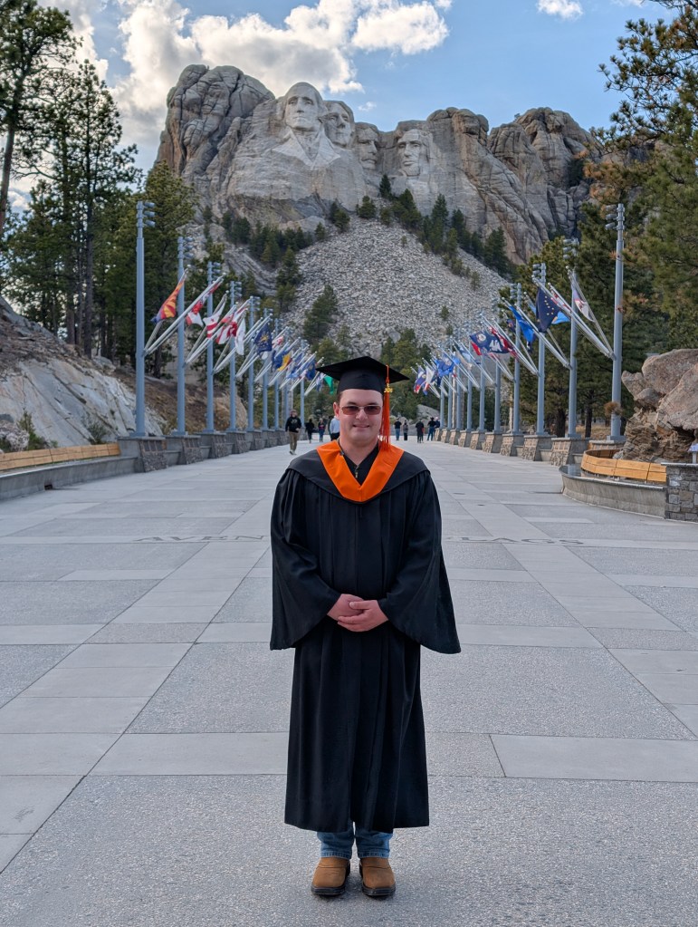 Clay Sabrowski pictured in his graduation regalia with Mt. Rushmore in the background