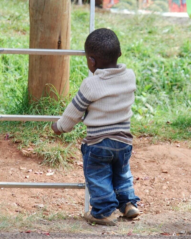 A child stands outdoors holding onto a metal ladder frame near a grassy area.